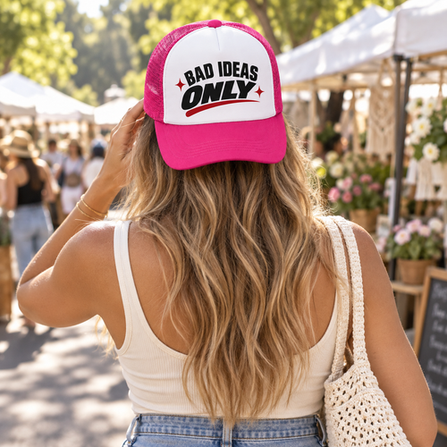 Woman wearing a pink Bad Ideas Only trucker hat at an outdoor market